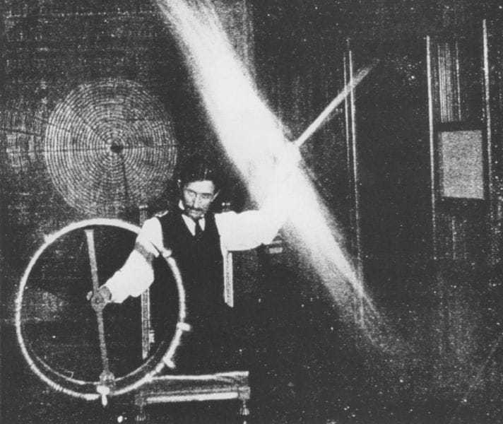 Tesla's body, in this experiment, is charged to a high potential by means of a coil responsive to the waves transmitted to it from a distant oscillator. A long glass tube waved in the hand is lighted to great brilliancy by the electrical charges conveyed to it through the body.